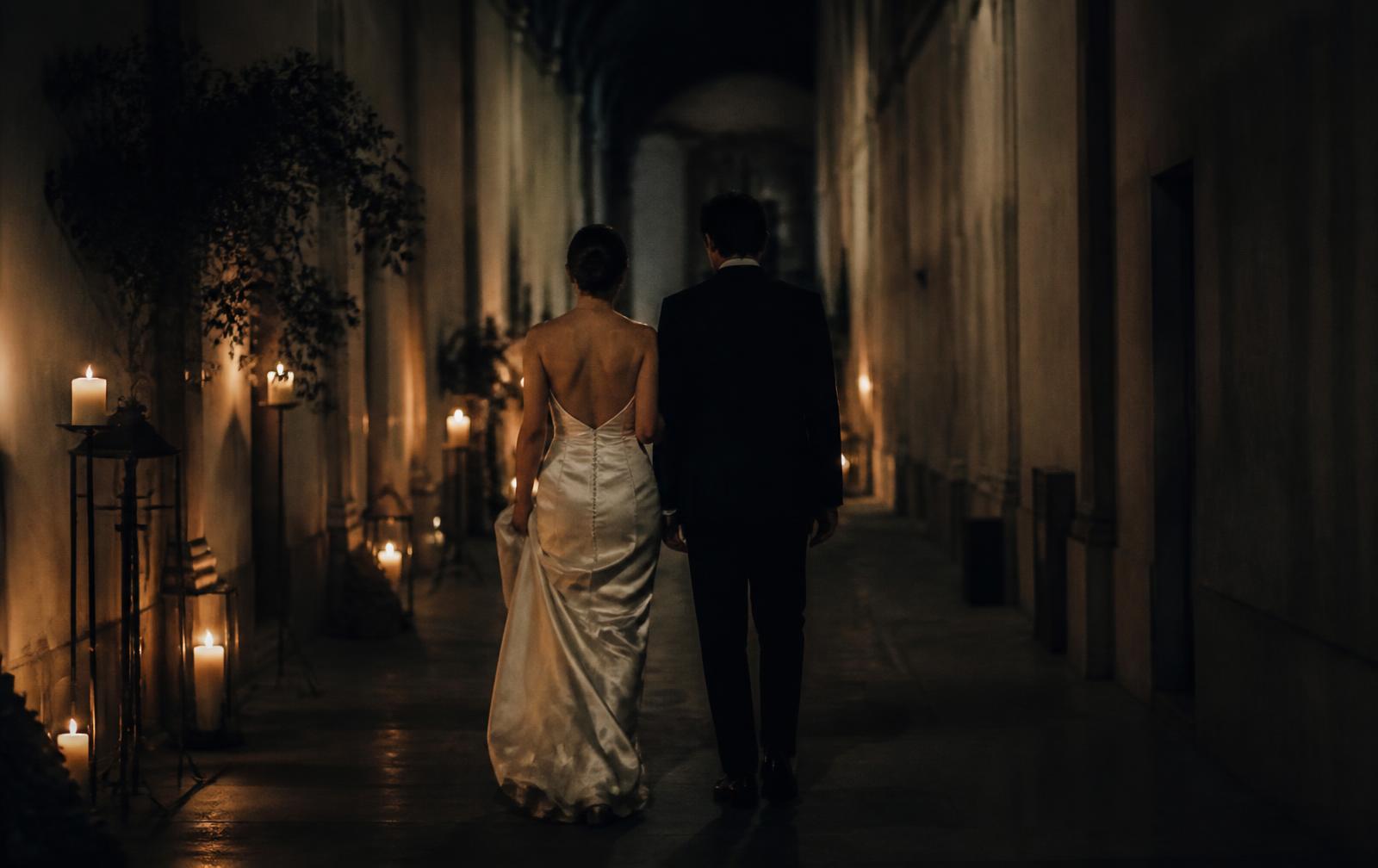 A couple walking away down a candlelit corridor